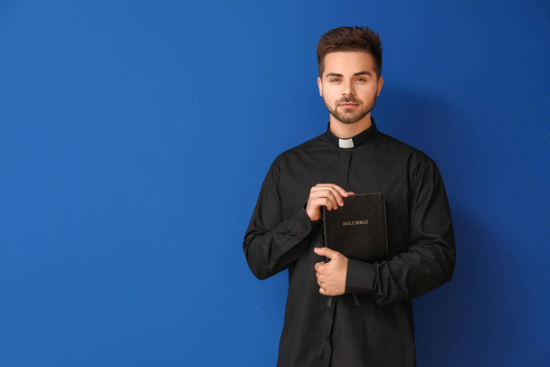 Jovem sacerdote com a Bíblia sobre fundo de cor
 - Foto, Imagem
