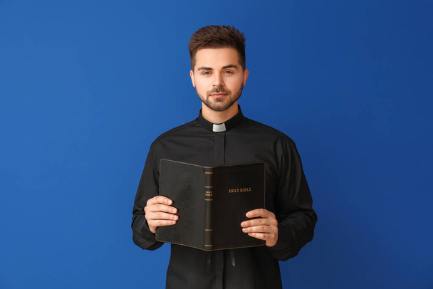 Young priest with Bible on color background - Φωτογραφία, εικόνα