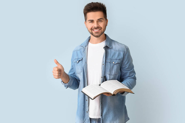 Νεαρός άνδρας με τη Βίβλο δείχνει αντίχειρα-up χειρονομία στο φόντο χρώμα - Φωτογραφία, εικόνα