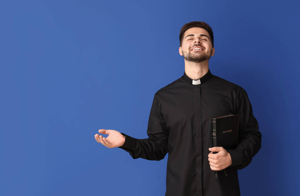 Young priest with Bible on color background - Photo, Image