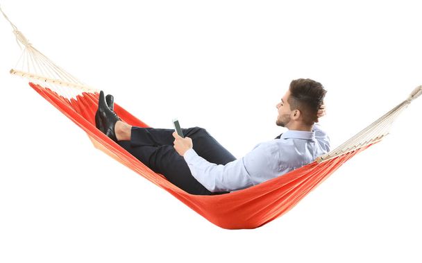 Young businessman with mobile phone relaxing in hammock against white background - Фото, изображение