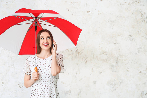 Beautiful woman with umbrella talking by mobile phone on light background - Photo, Image