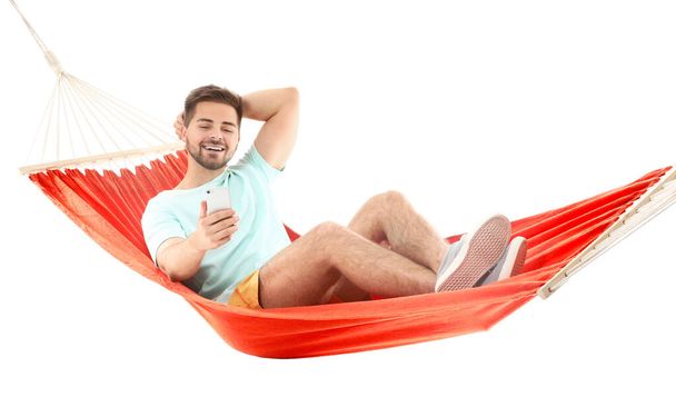 Hombre joven con teléfono móvil relajante en hamaca sobre fondo blanco
 - Foto, Imagen