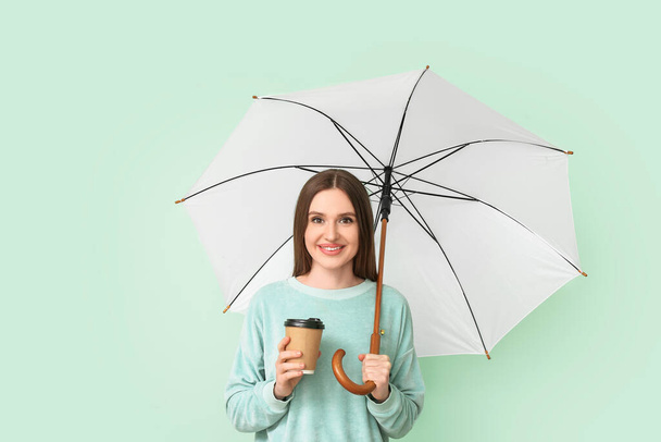 Schöne Frau mit Regenschirm und Tasse Kaffee auf farbigem Hintergrund - Foto, Bild