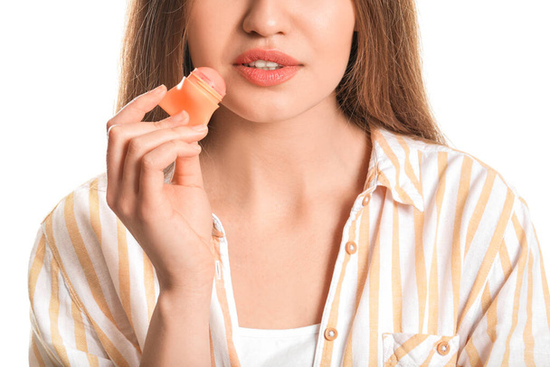 Mooie jonge vrouw met lip balsem op witte achtergrond, close-up - Foto, afbeelding