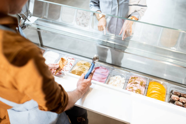 Salesman picking ice cream with a spoon from refrigerator in the shop - Photo, Image