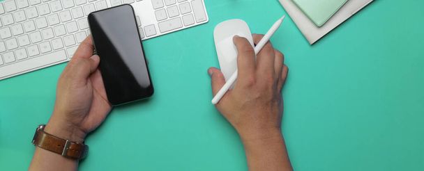 Накладний знімок чоловічого підприємця правою рукою за допомогою комп'ютерного пристрою та лівої руки, що тримає смартфон на робочому столі
 - Фото, зображення