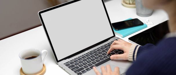 Oříznutý záběr pracovnice na notebooku s kancelářským stolem s digitálním tabletem, smartphonem a kancelářskými potřebami  - Fotografie, Obrázek