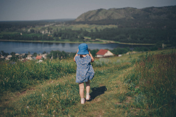 child against the background of wild nature. Russian mountains, plains, fields. the girl in the tall grass and looks into the distance - Valokuva, kuva