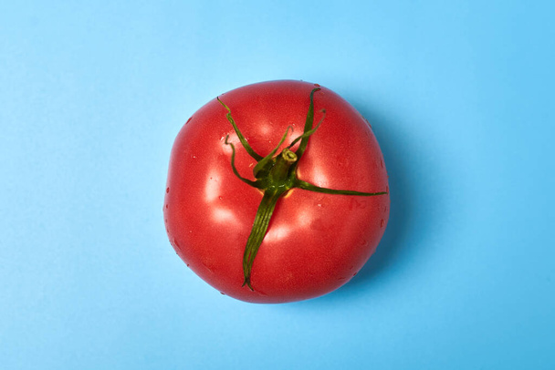 Whole appetizing red tomato on a blue background. - Фото, изображение