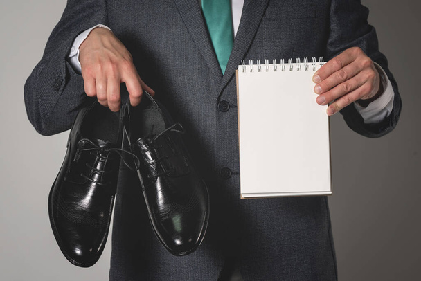Shoe care tips mock up. Business man holding in hands a new pair of black shoes and a blank page notepad with a copy space. - Photo, image