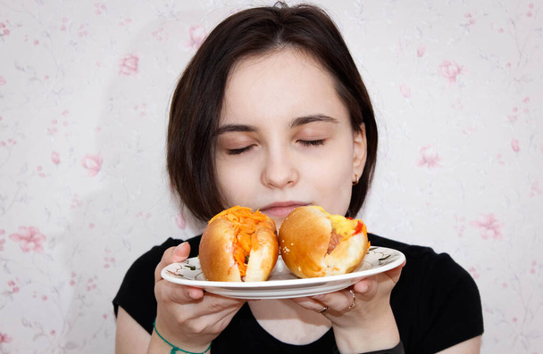 Een mooi meisje houdt een bord hotdogs in haar handen en ruikt ze met plezier. Close-up, selectief schot. - Foto, afbeelding