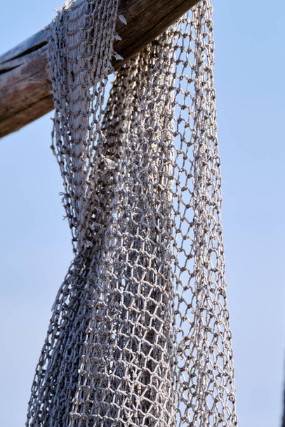 Рыболовные сети висят на деревянной балке. На фоне голубого неба. Натюрморт и предметы. Рыбаки, рыболовные сети
. - Фото, изображение