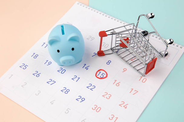 Sezónní slevy. Piggy banka s kalendářem, supermarket vozík na barevném pozadí - Fotografie, Obrázek