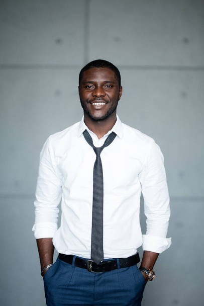 Portrait of a black man in a white shirt standing with his hands in his pockets and smiling at the camera. - Foto, Bild