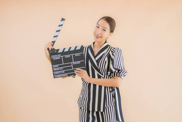 Portrait beautiful young asian woman with movie clapper on brown background - Photo, Image