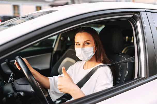 Woman with medical mask is driving a car - Foto, imagen