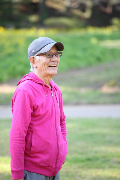 senior Japanese man in a hoodie smiles outdoor - Фото, изображение