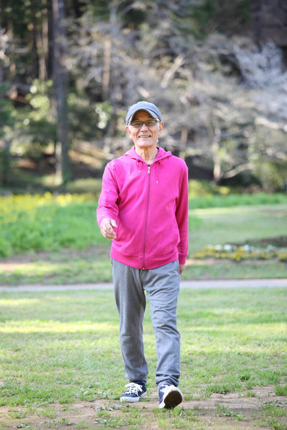 senior Japanese man in a hoodie walks on a lawn - Foto, afbeelding