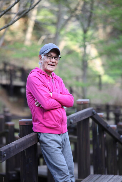 senior Japanese man in a hoodie standing on the wooden deck at natural park - Fotó, kép