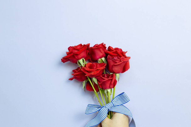 Ruka drží červené růže květiny na fialovém pozadí. Květinová kompozice, plochý ležel, horní pohled, kopírovací prostor - Fotografie, Obrázek