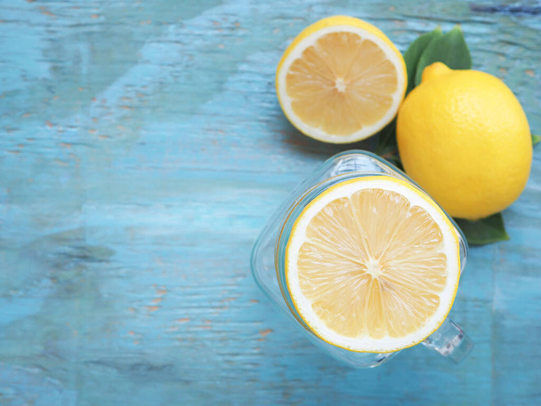 Vista superior, rebanada de limón fresco puesta en tarro y la mitad con hojas sobre fondo de madera azul. Copiar espacio
 - Foto, Imagen
