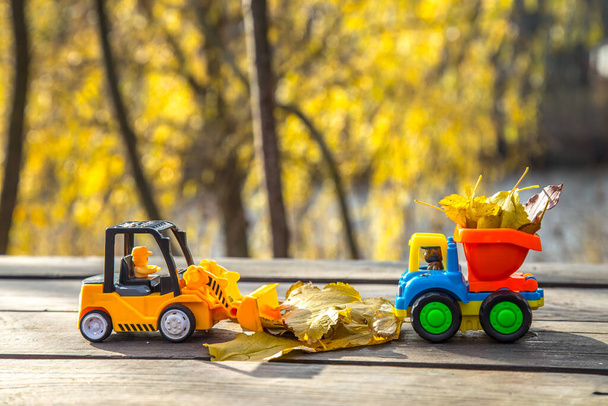 Malé autíčko a traktor stojí na dřevěném povrchu na pozadí rozmazaného podzimního parku. - Fotografie, Obrázek