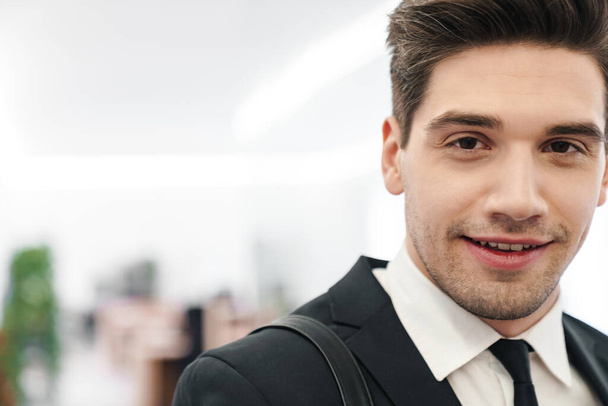 Image closeup of happy young businessman wearing black suit smiling while standing in office - Φωτογραφία, εικόνα