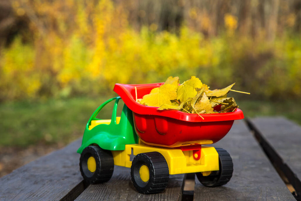 El pequeño coche de juguete se encuentra sobre una superficie de madera sobre un fondo de un parque de otoño borroso
. - Foto, imagen