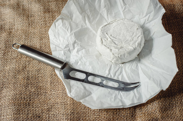 Camembert cheese, French soft cheese with white mold on kraft paper for cheese ripening, closeup. Cheese slicing knife. - Photo, Image