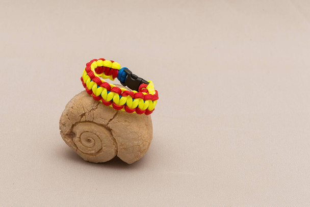 Colorful paracord bracelet placed near a fossilized shell,  isolated on a light brown background; presentatio - Photo, Image