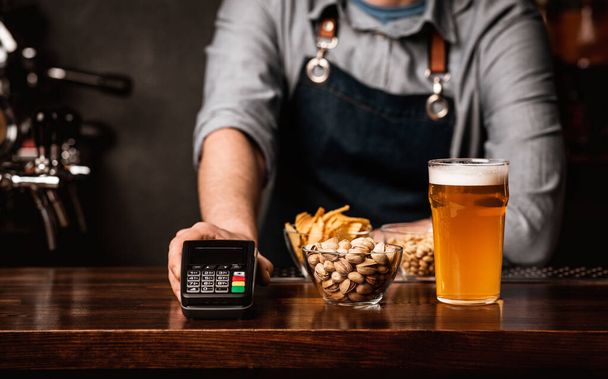 Bartender serves glass of beer, snacks and modern terminal - Photo, Image