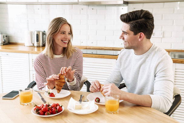 Retrato de pareja feliz joven comiendo juntos en la mesa mientras desayunan en la acogedora cocina en casa - Foto, imagen