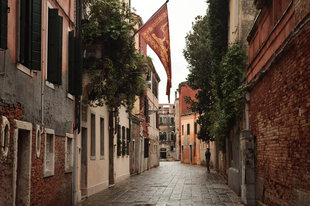 Eski bir evin cephesinde asılı bir bayrak olan Venedik caddesi. İtalya. - Fotoğraf, Görsel