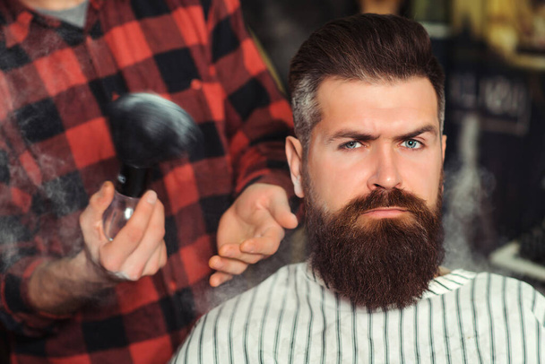 Bearded man getting haircut by hairdresser. Brutal guy sitting in barber chair. Man making haircut to look perfect. Stylish bearded man in salon. New perfect style. Beard styling and cut. - Φωτογραφία, εικόνα