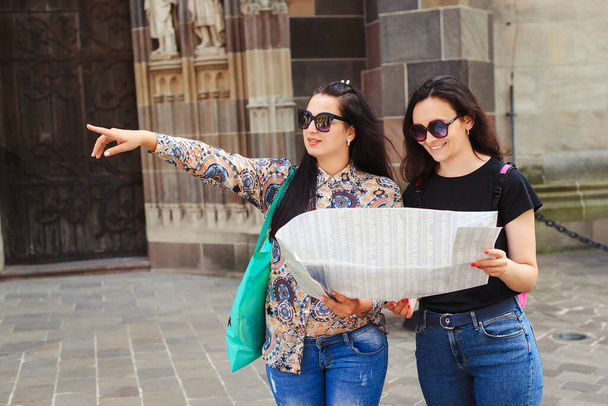 Młodzi, szczęśliwi przyjaciele zwiedzają miasto. Przyjaźń i koncepcja podróży. Dwie kobiety czytające mapę na ulicy. Modne dziewczyny spacerujące po Europie nowoczesne centrum miasta. Travle, styl życia, wakacje. - Zdjęcie, obraz