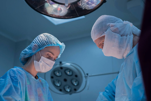 Children's surgeons perform urological operations. A man and a woman in a mask and a blue sterile coat in the operating room. A team of surgeons is conducting an operation. Treatment of inguinal hernia, testicular edema, testicular disease, varicocel - Photo, Image