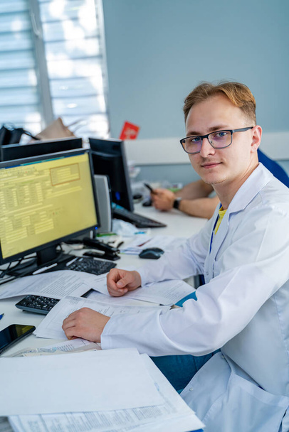Doctor in medical office. Medic sits at computer. Man in scrubs. - Fotoğraf, Görsel