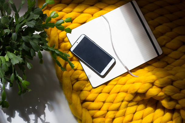 Blank open notepad with smartphone  in home office on yellow blanket background with green plant - 写真・画像