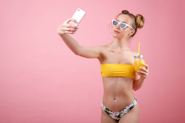 Uma rapariga de fato de banho e óculos com sumo tira uma selfie. humor de verão
 - Foto, Imagem