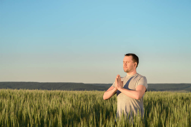 Un hombre adulto se para en un campo de hierba alta haciendo yoga durante el atardecer
. - Foto, Imagen