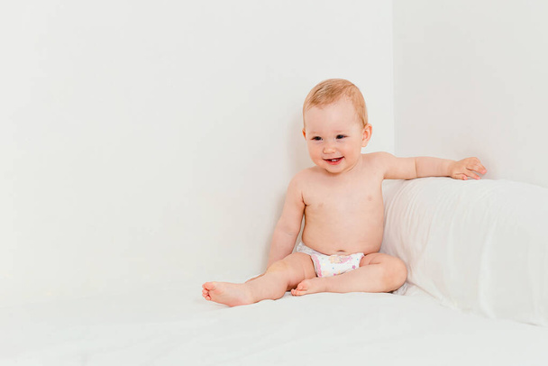 Ten-month-old smiling baby in a diaper sits on a bed - Photo, image