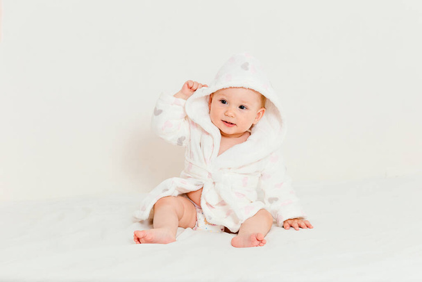 Baby in a bathrobe after bathing sits on a bed on a white background - Foto, immagini