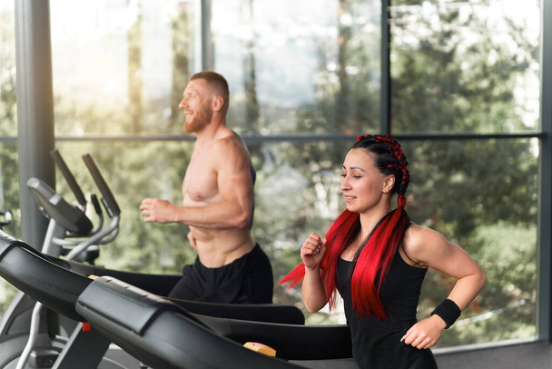 Gym treadmill running trainer man woman training together jogging fitness workout Warming up before functional cross training Personal coach train girl run on treadmil with panoramic window background - Foto, immagini