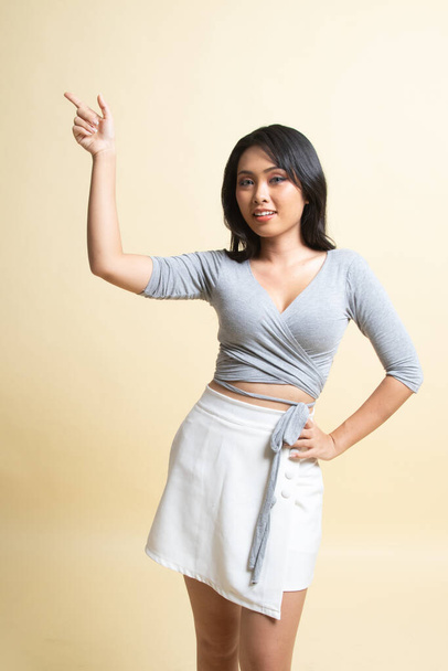 Young Asian woman smile and point   on beige background - Foto, Imagen