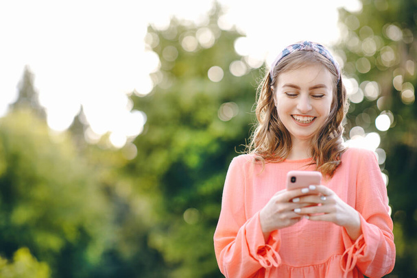 Dziewczyna korzystająca ze smartfona na świeżym powietrzu i zielonym tle natury. Dziewczyna trzyma smartfona. Kobieta korzystająca ze smartfona w pięknym zielonym parku - Zdjęcie, obraz