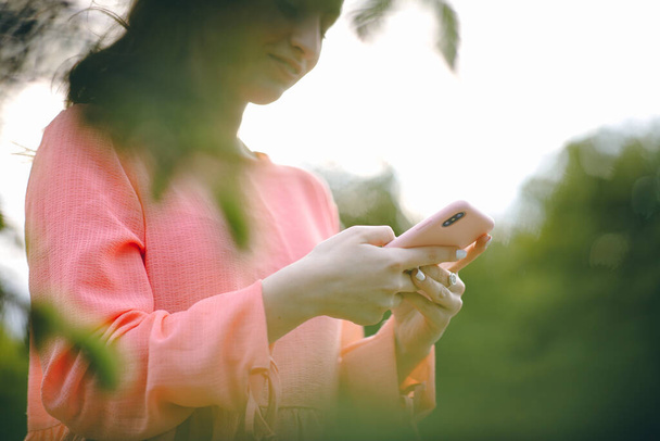 屋外や緑の自然背景でスマートフォンを使用して女性。女の子の手をスマートフォンを保持。美しい緑の公園でスマートフォンを使用して女性. - 写真・画像