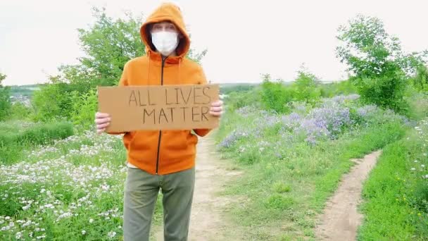 Młody człowiek w masce z kartonowym plakatem w ręku z napisem - WSZYSTKIE ŻYCIE ma znaczenie. Jeden protest. - Materiał filmowy, wideo