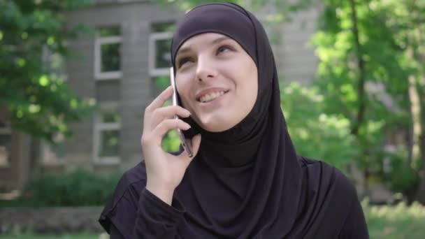 Close-up face of excited muslim woman talking on the phone outdoors. Portrait of happy cheerful young Middle Eastern girl using smartphone. Joy, lifestyle, communication. - Footage, Video