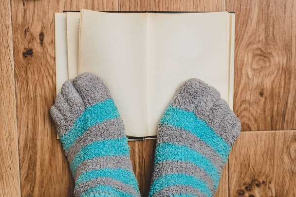 Csíkos zokni lábujjakkal a háttérben egy nyitott könyv a fa padlón. Kényelmes ruházat a lábaknak a hétvégén. - Fotó, kép